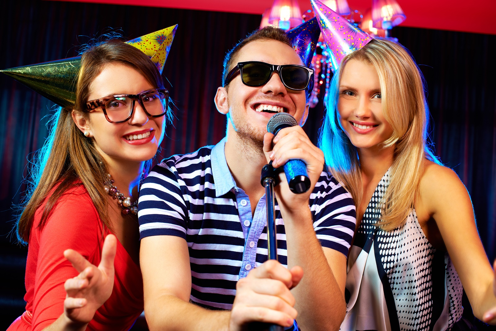 Portrait of happy friends singing in microphone in the karaoke b